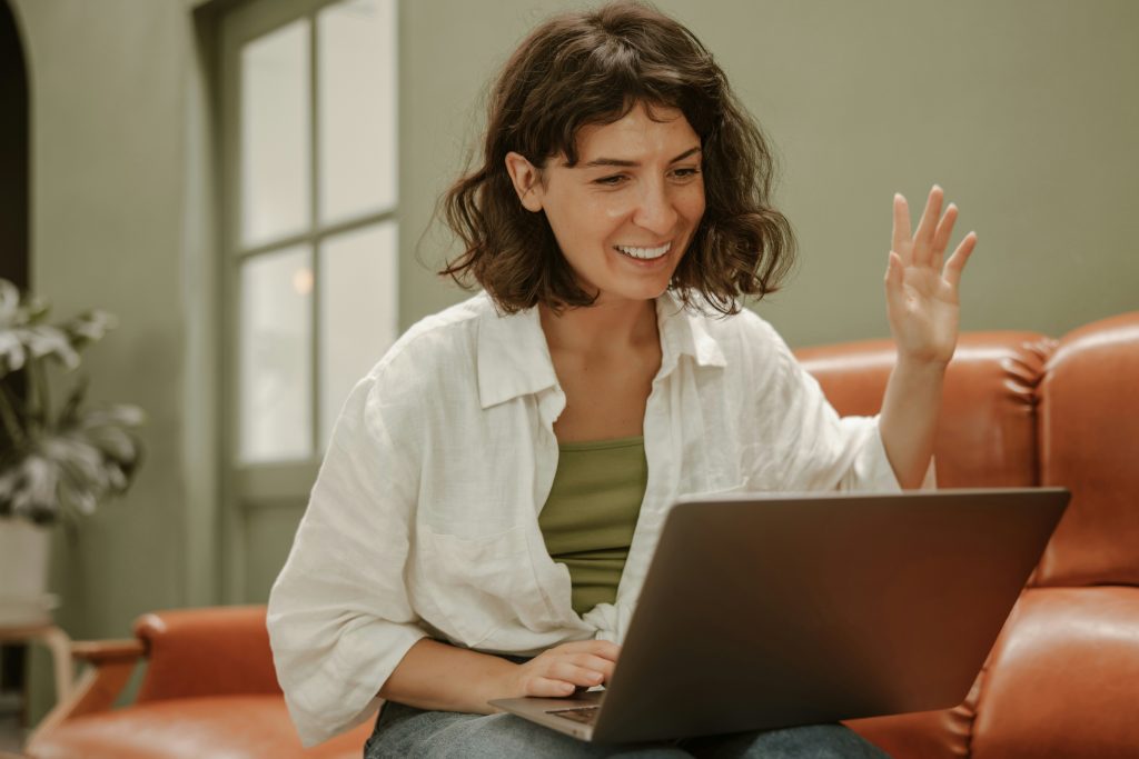 femme souriant et saluant en visio sur son PC